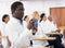 Interested African American in white coat using smartphone at lecture