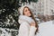 Interested long-haired woman in white attire enjoying happy winter time and laughing. Outdoor portrait of magnificent