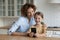 Interested mom sit by table with little daughter using cellphone