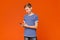 Interested teen boy using smartphone on orange background