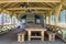 Interior of beautifully decorated modern open wooden pavilion with beam ceiling and walls, massive table, benches and big stone fi