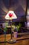 Interior cafe with desk lamp with sconces and red tulip in glass vase and small bouquet of flowers on wooden table