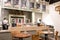 Interior of cafe showing laid wooden tables with cutlery in shabby chic rustic styled eating area with counter and serving area b