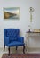 Interior composition of retro blue armchair, vintage wooden beige table, table lamp, books, and pendulum clock over off white wall