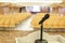 Interior of a conference room. Detail of a microphone sitting on a desk facing the room full of tables and chairs