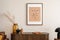 Interior design of living room interior with mock up poster frame, wooden commode, glass vase with dried flowers, brown sofa, book