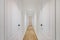 Interior of long narrow hallway with closed doors, wooden floor and white walls in apartment designed in minimal style