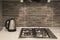 Interior of a modern kitchen. Close-up of electric kettle and gas hob on grey tile backsplash