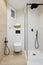 Interior of modern style bathroom in white and beige colors in refurbished apartment. Shower zone and toilet, with black