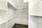 Interior of a plain white walk in closet with shelvings and carpeted floor