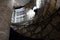 Interior shot of looking up a spiral staircase made out of stone with handrail, lamp providing light and window