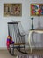 Interior shot of vintage rocking chair, old style table, candlestick on background of off white wall with two hanged paintings