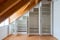 Interior view of a custom-made closet with open doors built into a master bedroom with a sloping roof