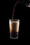 International Beer Day. Stout ale being poured in to a pint glass. Against black background.