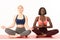 International girls in sportswear sitting in lotus position, african and european female`s meditating with closed eyes