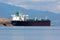 International oil tanker waiting in local harbour to be unloaded surrounded with calm blue sea and stone shore with mountains and