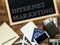 Internet marketing handwritten with white chalk on a blackboard, money wallet , notebook and smartphone on a wooden background