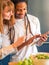 Interracial couple formed by African and Caucasian prepare a salad together with the help of their cell phone