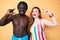 Interracial couple wearing swimwear smiling and confident gesturing with hand doing small size sign with fingers looking and the