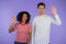 Interracial friendly couple - white man and african woman waving hands - hello. Greeting, say Hi to camera on purple