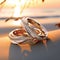 Intertwined Wedding Rings with Diamonds and Pearls on a Sun-Kissed Beach at Sunset