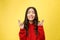 Intrigued woman in praying with crossed fingers and looking away over yellow background