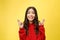 Intrigued woman in praying with crossed fingers and looking away over yellow background