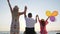 Invalid with wife and daughter raise their hands up with colorful air balloons near sea, family with child