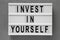 `Invest in yourself` words on a lightbox over gray background, top view. Overhead, flat lay, from above. Close-up