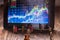 Investment graphics on screen with miniature people watching