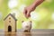 Investor hand hold a coin with save in the piggy bank put on the money on home model for family background.