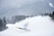 Invisible skier skiing and jumping high up in deep snow powder. Dark wooded mountains view in snowfall on background.