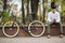 Inviting friend for a ride. Happy young indian bearded man talking on the mobile phone and smiling while sitting near his bicycle