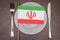 The Iranian flag lies on a plate between a knife and fork. Concept: political ambitions, division of the country, intervention fro