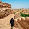 Iranian woman wearing a traditional dress, known as a chador, walks up a hill with the city of Yazd in the background