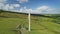 Ireland green farmland windmill aerial view: blades spin, power plant with solar panels in meadow