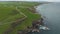 Ireland ocean coastal meadows aerial view: road with cars at green landscape. Waves of rocky bay