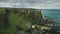 Irish castle cliff shore aerial view: Dunluce on green grass valleys and meadows at ocean bay