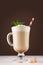 Irish coffee with cream, fresh mint and striped red straw in transparent glass with handle on white wood board in brown color.