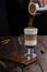 Irish coffee in transparent glass on wooden table. Barista`s hand sprinkles cinnamon on white foam. Coffee mood concept with copy