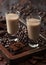 Irish cream baileys liqueur in shot glasses in wooden tray with coffee beans and powder with dark chocolate on dark wood