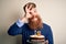 Irish redhead man with beard holding birthday cake with burning candles over isolated background with happy face smiling doing ok