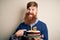 Irish redhead man with beard holding birthday cake with burning candles over isolated background with surprise face pointing