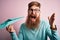 Irish redhead man with beard holding paper plane over pink isolated background very happy and excited, winner expression