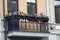 Iron balcony and flowerpots with red flowers with a window on a brown wall