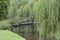 Iron bridge over river under weeping willow, summertime day .