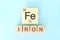 Iron chemical element symbol with atomic mass and atomic number in wooden blocks flat lay composition.