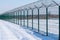 Iron fence with barbed wire in a snow-covered winter field against a blue sky. Fenced guarded territory, no access. Area