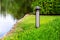 An iron garden lighting lantern mounted on a green lawn with bushes.