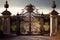 iron gates at the entrance to a grand and opulent mansion, with manicured grounds and rolling hills in the background